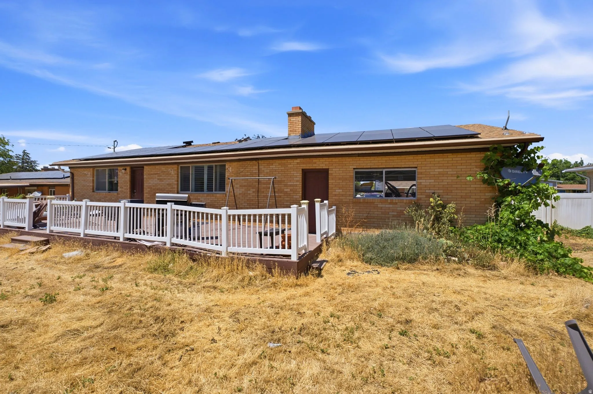 Brick exterior featuring a wood deck with white railings, multiple windows, solar panels, and a brown roof