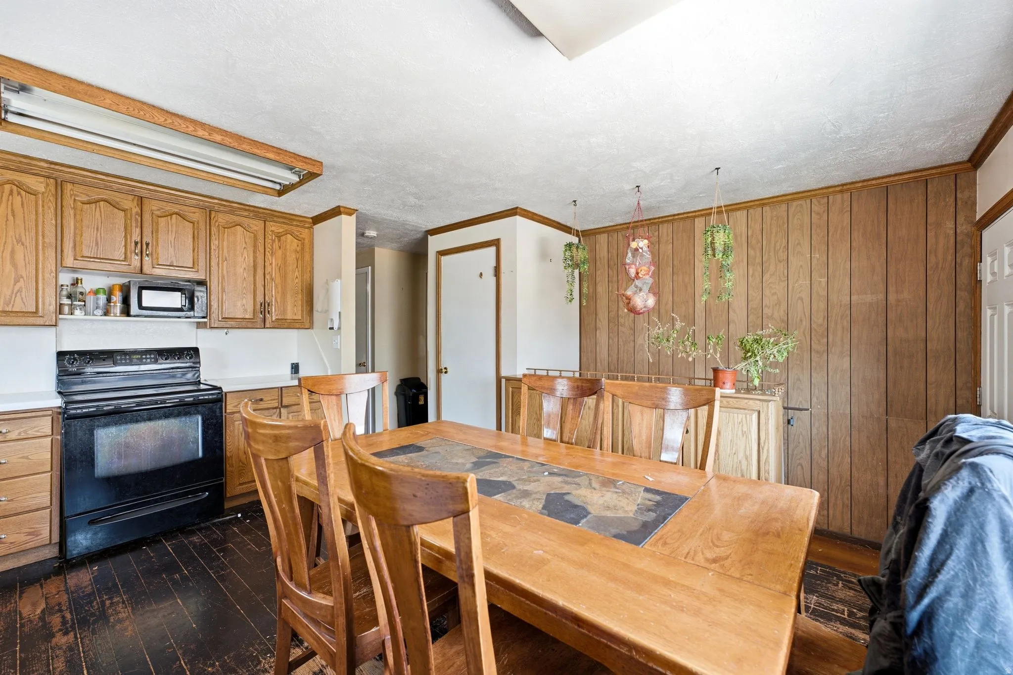 Kitchen and dining area featuring wood cabinetry, white countertops, black oven, paneling detail, and dark wood-finish flooring