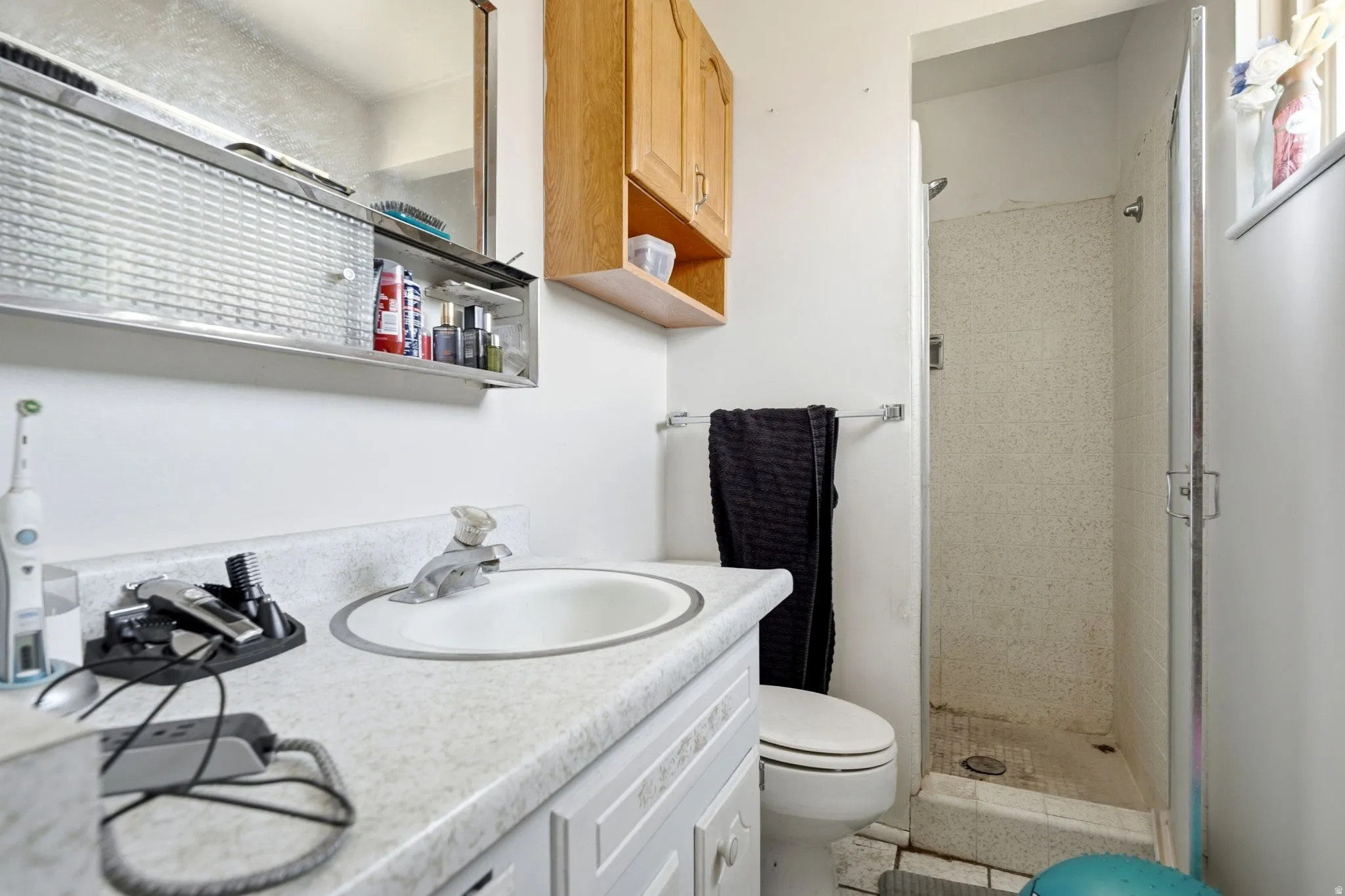 Bathroom featuring a single vanity with an integrated sink, a built-in medicine cabinet, a light wood-finish wall cabinet, a toilet, and a tiled shower stall with a glass door