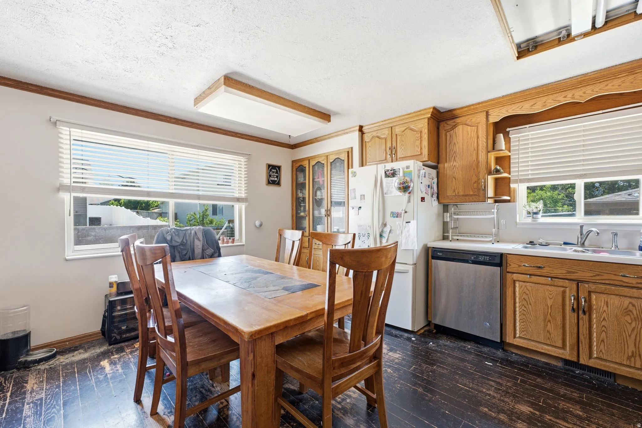 Kitchen and dining area featuring wood-finish cabinetry, stainless steel dishwasher, white sink, and dark wood-finish flooring