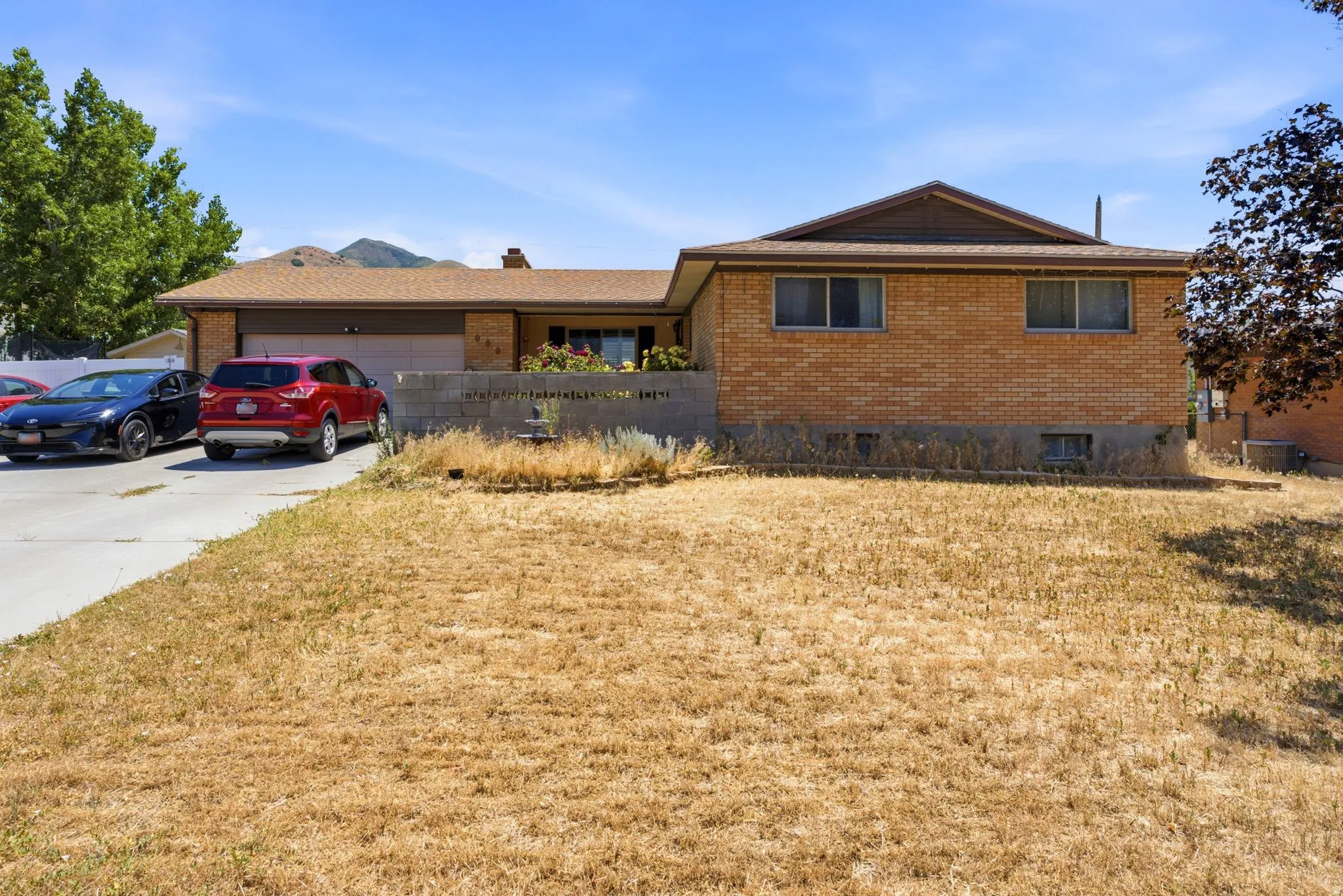 Brick exterior property with an attached two-car garage, a concrete driveway, and a raised planter bed