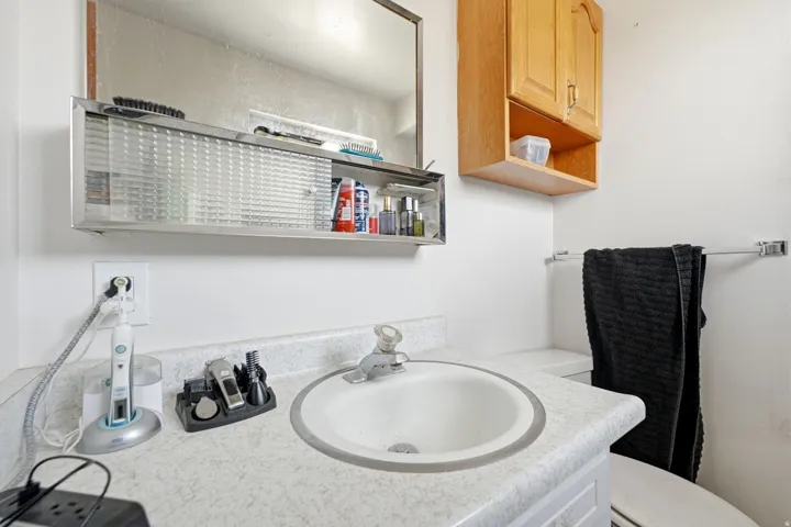 Bathroom vanity featuring a white drop-in sink, laminate countertop, and overhead medicine cabinet with frosted sliding doors