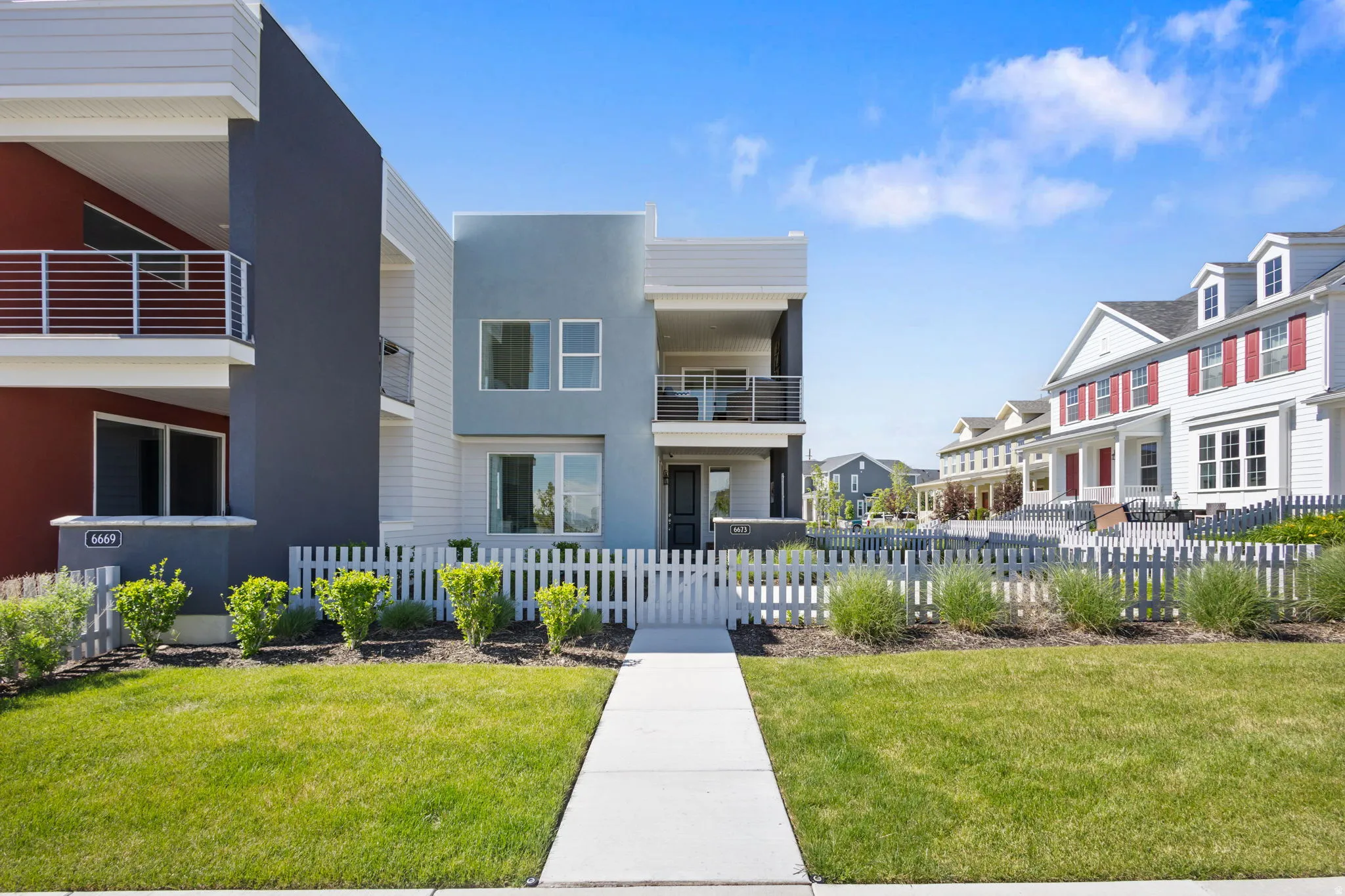 Contemporary exterior with multi-toned facade, multiple balconies, a white picket fence, a manicured lawn, and a concrete pathway