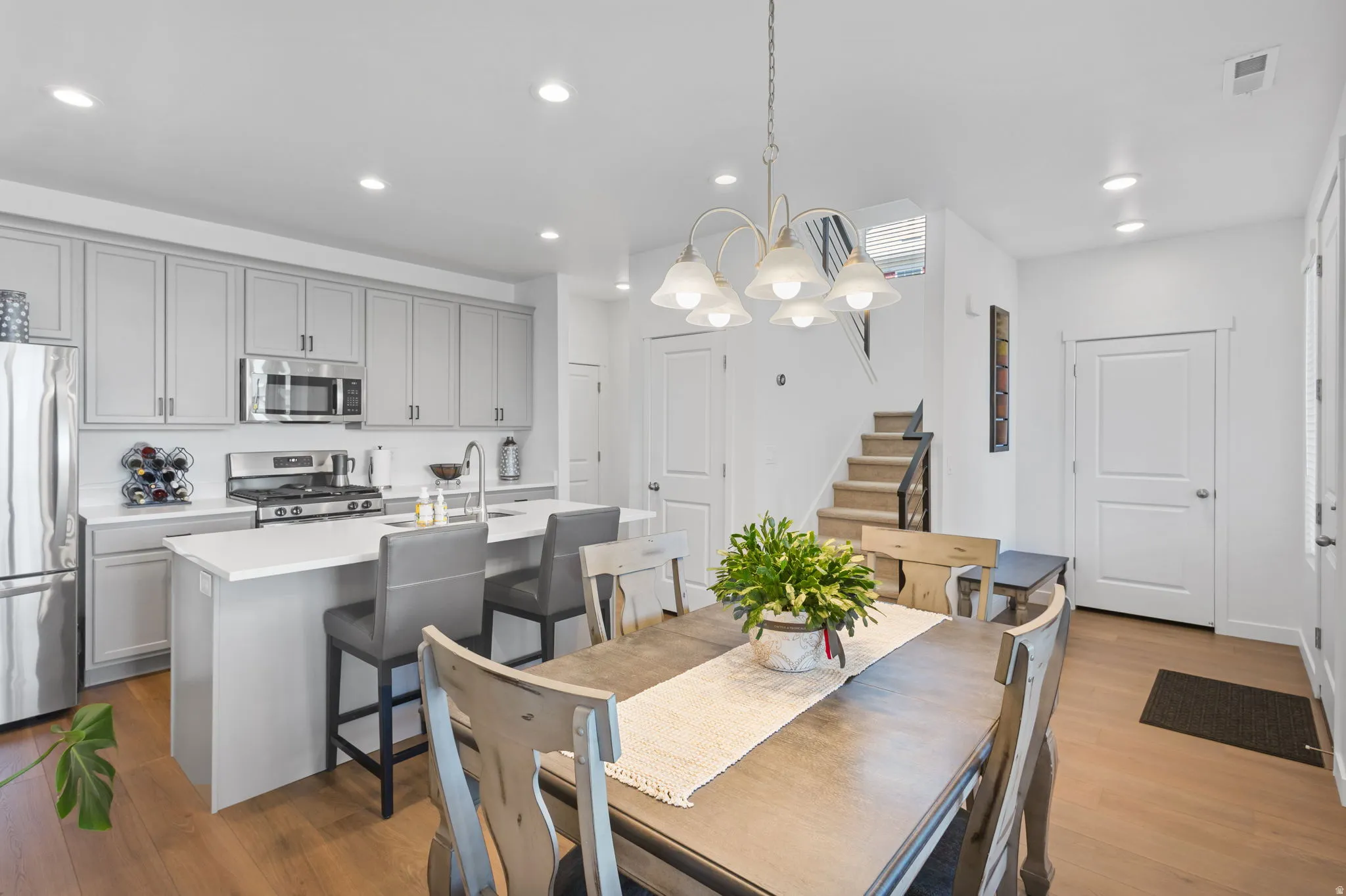 Open-concept kitchen and dining area featuring light wood-finish flooring, a kitchen island with seating, stainless steel appliances, and light gray cabinetry