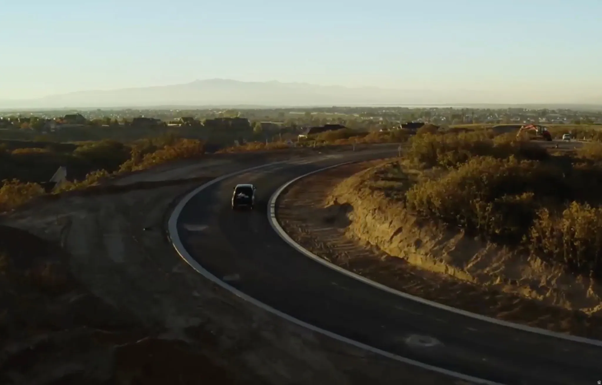 Curved paved road with concrete curbing, bordered by natural landscaping