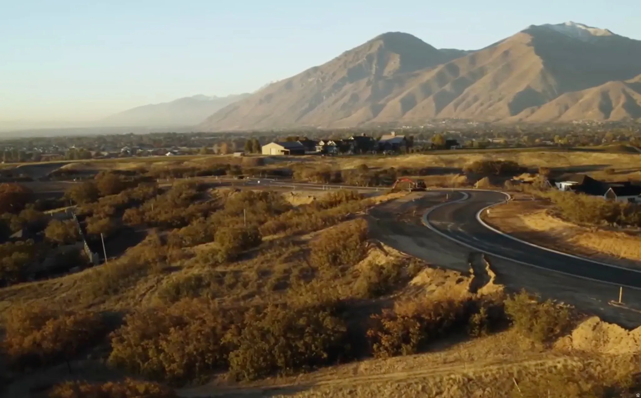 Expansive undeveloped land featuring a newly paved road, distant mountain range, and scattered low-growth vegetation