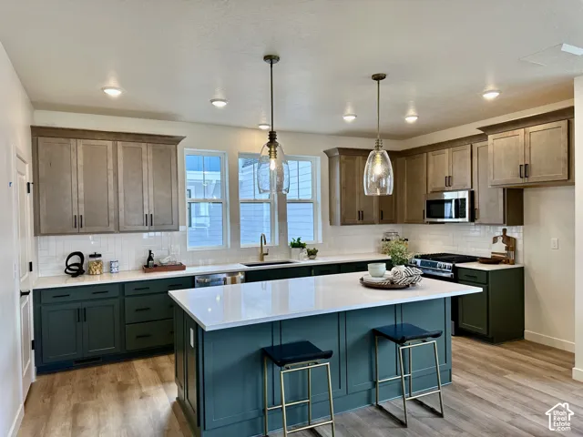 Kitchen featuring a spacious island with a white countertop, two-tone cabinetry, stainless steel appliances, and wood-finish flooring