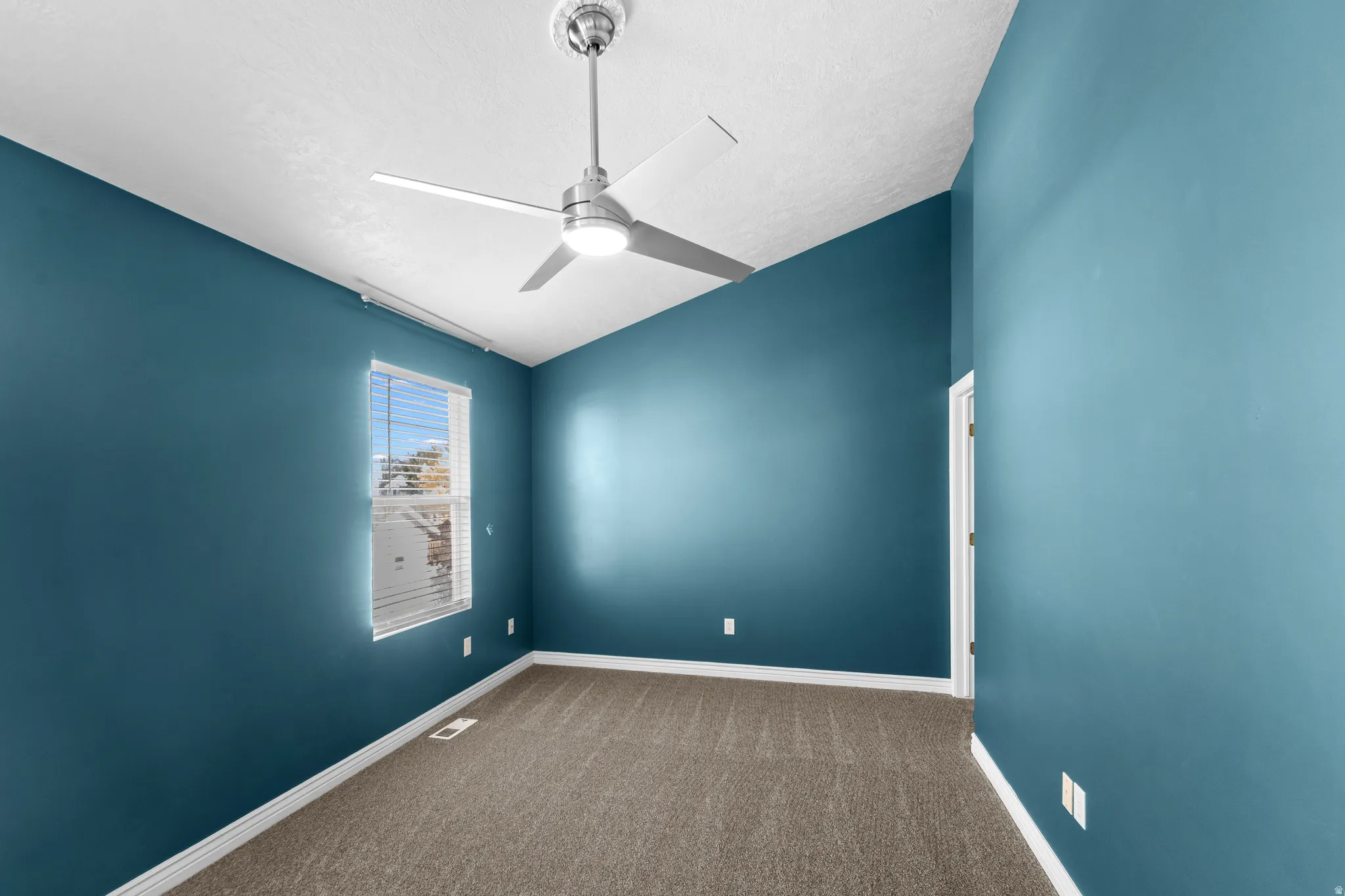 Vaulted ceiling bedroom featuring teal walls, textured carpet flooring, a window with blinds, a modern ceiling fan, and white trim