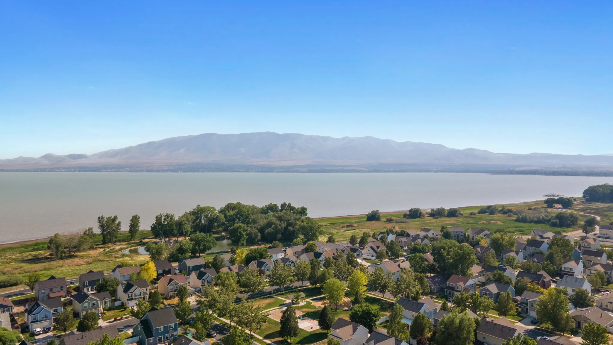 Aerial perspective showcasing a residential community bordering a large body of water with distant mountains