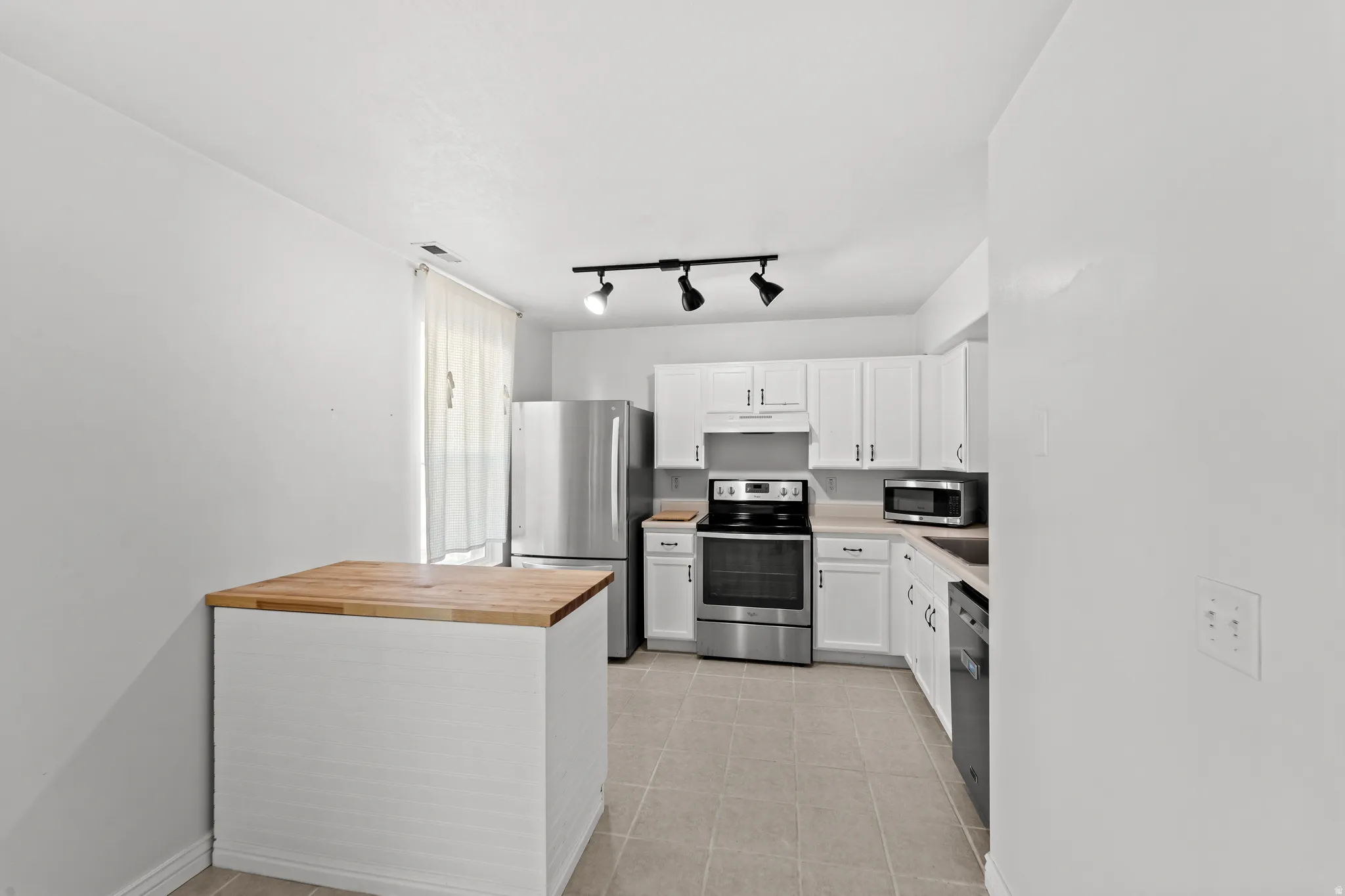 Kitchen featuring white cabinetry, stainless steel appliances, a wood-finish island, track lighting, and tile flooring