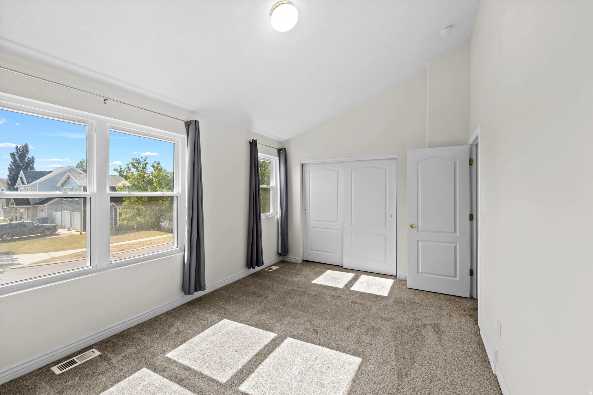 Carpeted room featuring a vaulted ceiling and multiple windows