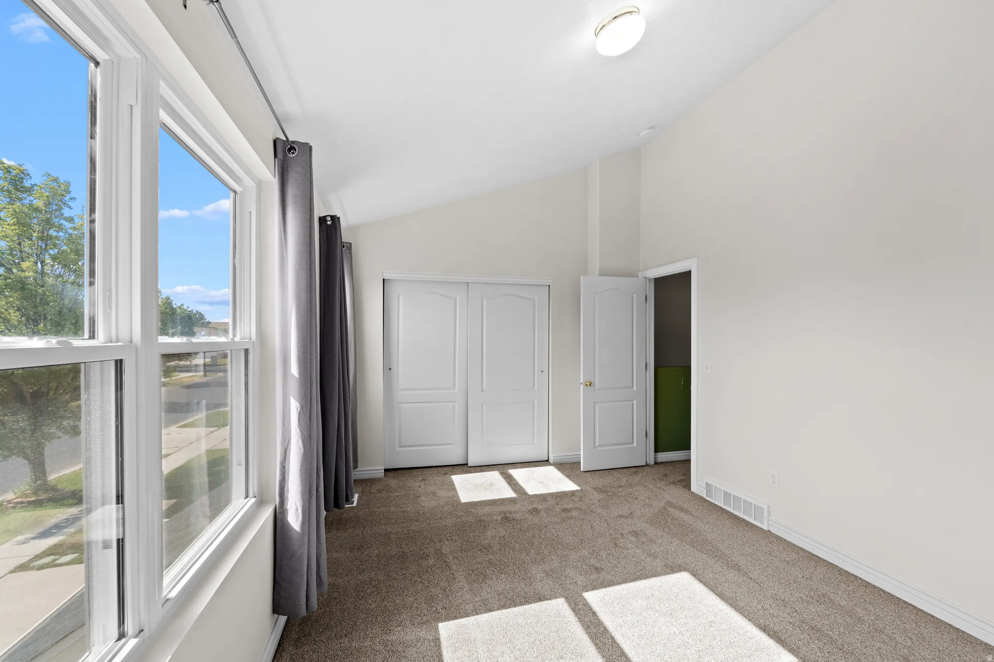 Bright interior space featuring a large multi-pane window, vaulted ceiling, neutral carpeting, white trim, and a flush-mount ceiling light