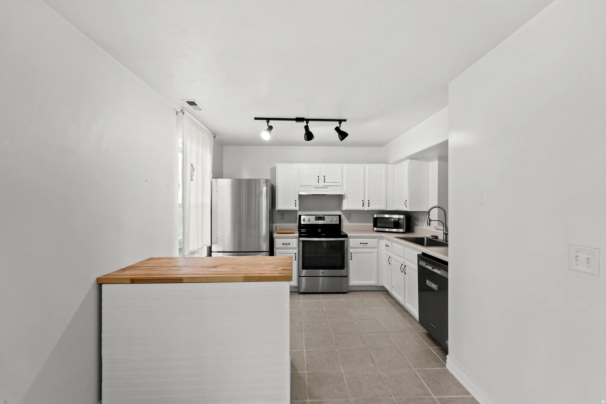 Kitchen featuring white cabinetry, stainless steel appliances, a black sink, a dishwasher, and track lighting