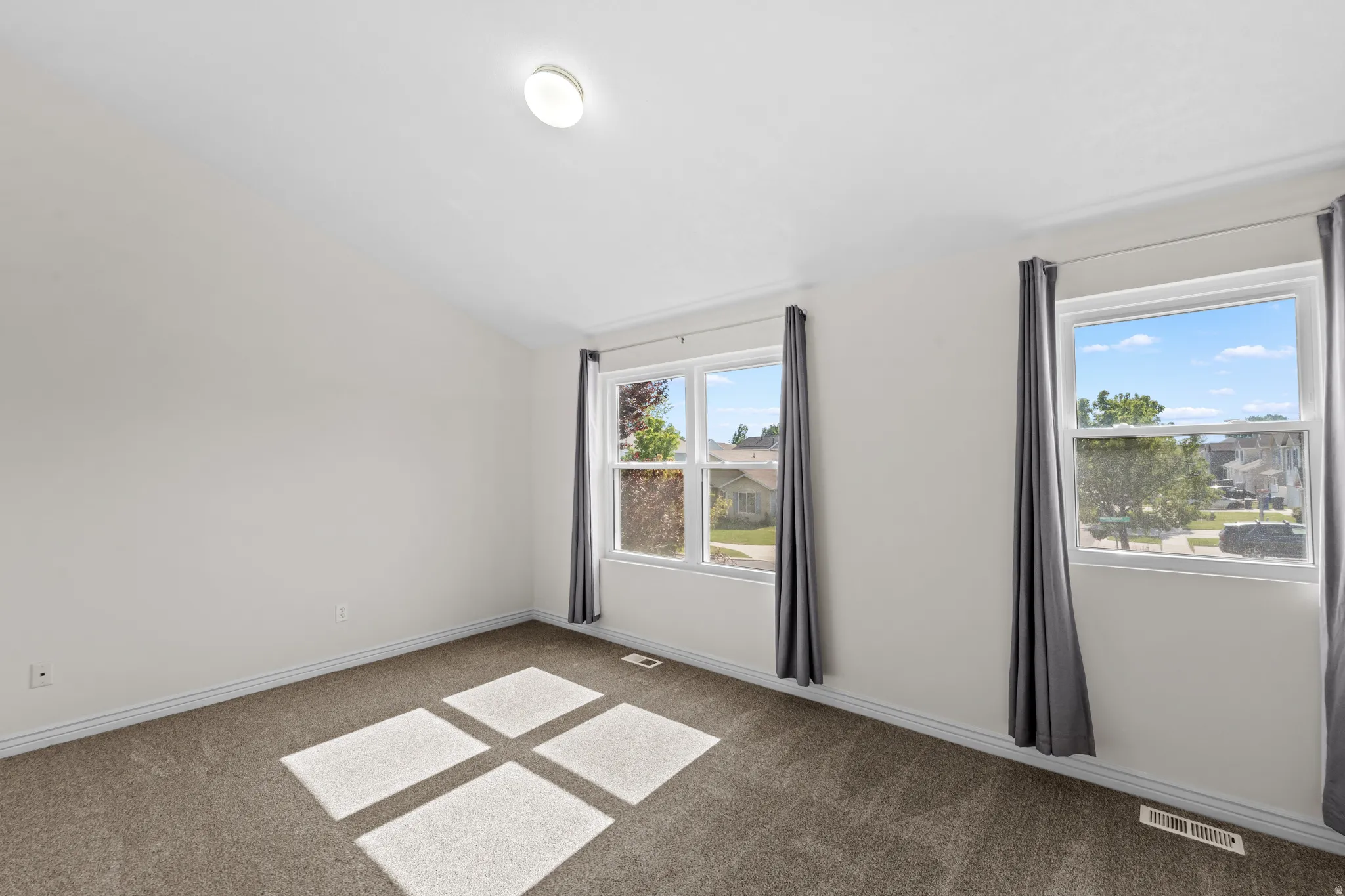 Bright room featuring two large windows, white walls, vaulted ceiling, and brown carpeting