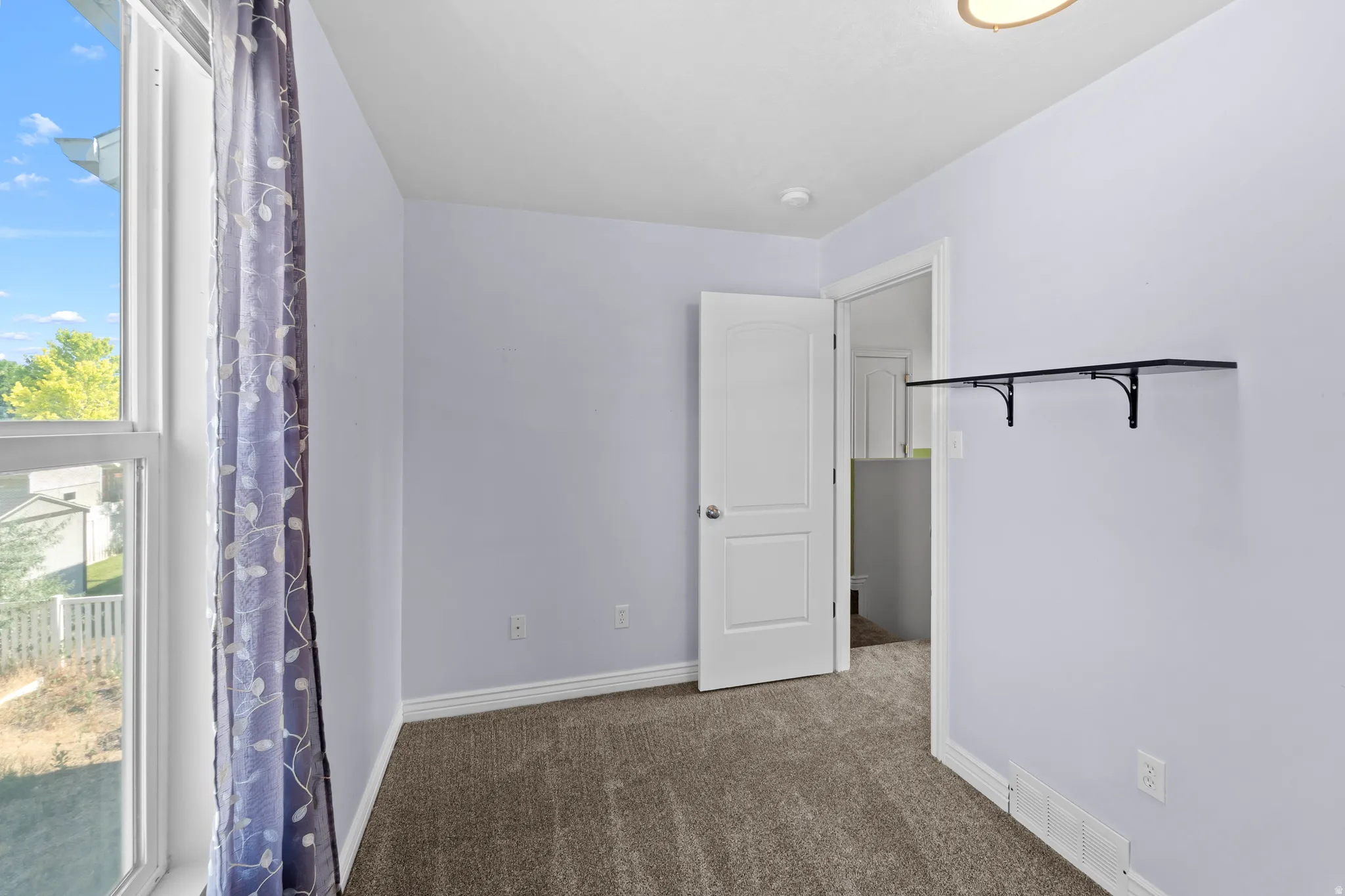 Bright room with a large window, neutral carpeting, and light-colored walls