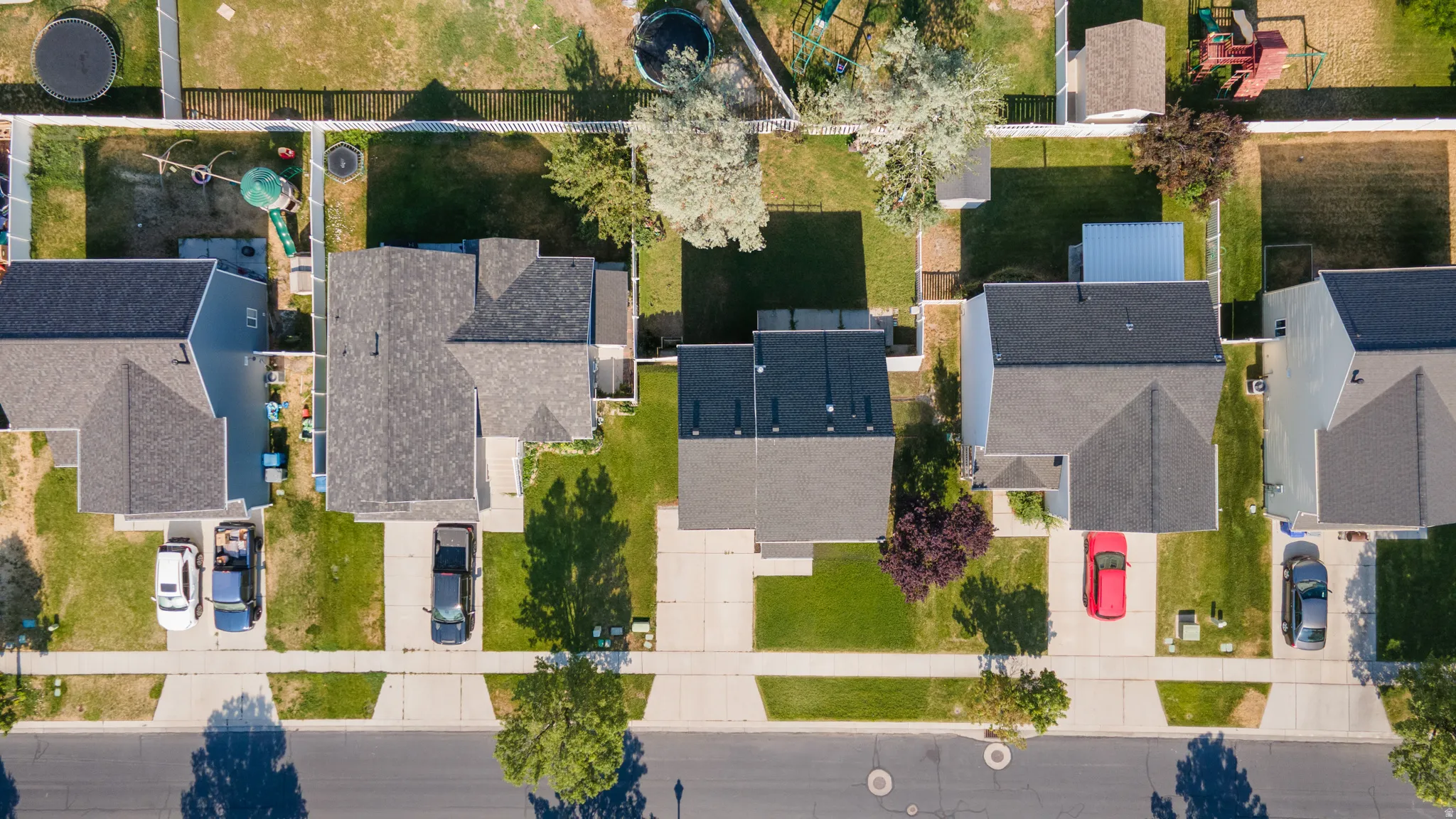 Aerial view showcasing multiple residential properties with pitched roofs, front driveways, and green lawns