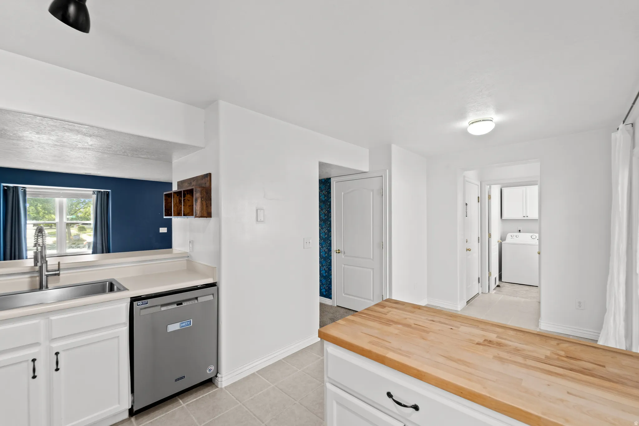 Kitchen featuring white cabinetry with dark hardware, a stainless steel sink with a high-arc faucet, and light-toned countertops