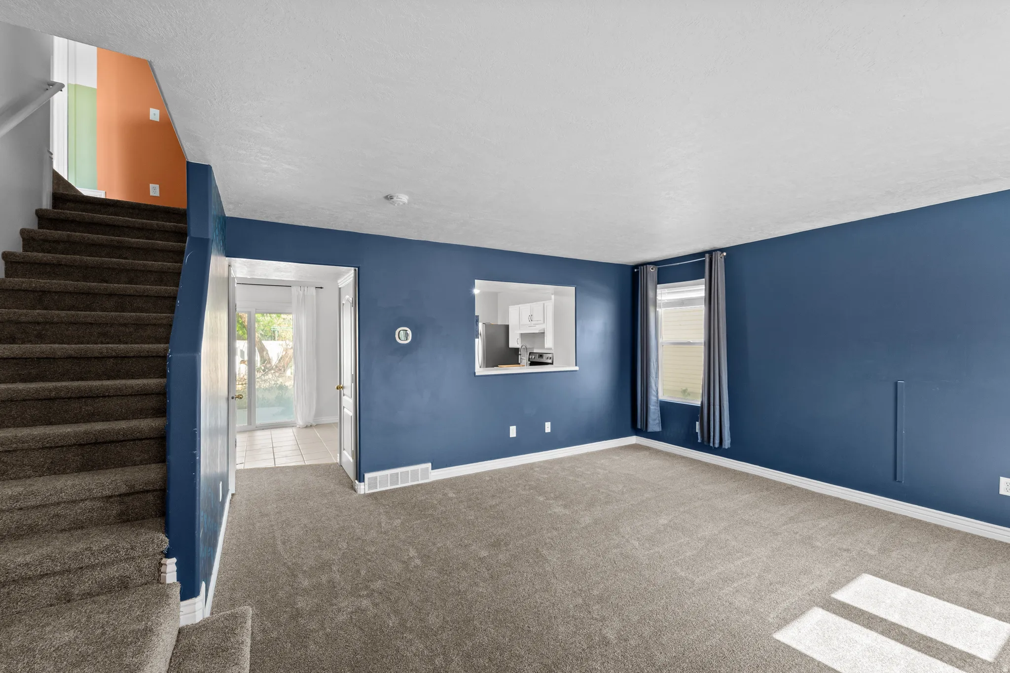 Carpeted living space featuring a pass-through window, a window with drapery, and a sliding glass door