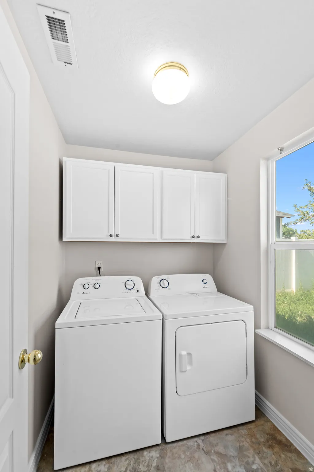 Dedicated laundry area featuring white upper cabinetry, a window, and a ceiling-mounted light fixture