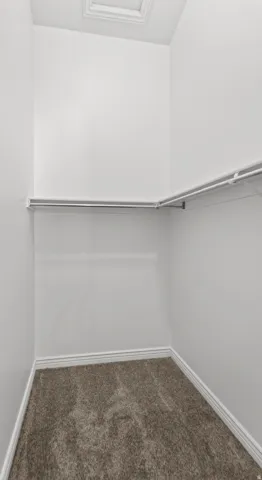 Carpeted interior closet featuring white walls, white trim, overhead access panel, and a metal hanging rod with an adjacent white wire shelf