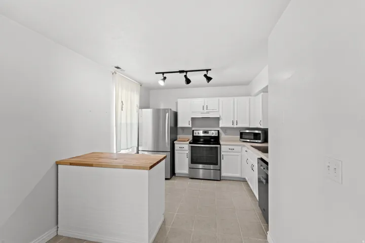 Kitchen featuring white cabinetry, stainless steel appliances, a wood-finish island, track lighting, and tile flooring