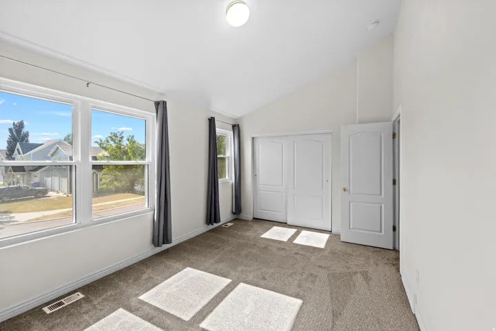 Carpeted room featuring a vaulted ceiling and multiple windows