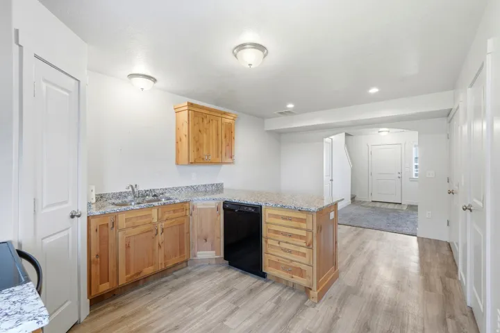 Kitchen featuring wood-finish cabinetry, granite-style countertops, a stainless steel sink, and a black built-in dishwasher