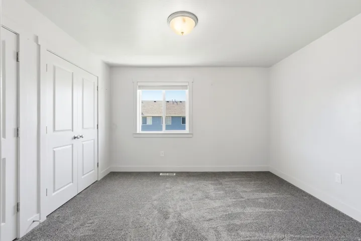 Neutral-toned room featuring a double-door closet, a single window, and grey patterned carpeting