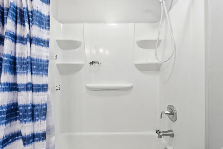 White fiberglass tub-shower combination featuring integrated shelving