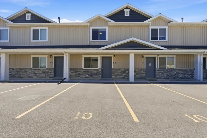Multi-unit residential facade featuring beige vertical siding, dark gray horizontal siding in the gables, and stone veneer accents