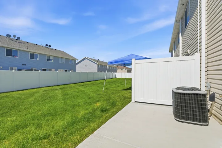 Expansive green space featuring a concrete patio, vinyl fencing, and tan horizontal siding