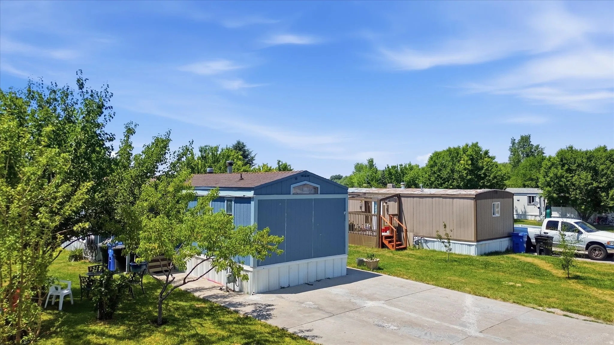 Blue exterior with white trim, featuring a paved driveway and surrounding green landscape