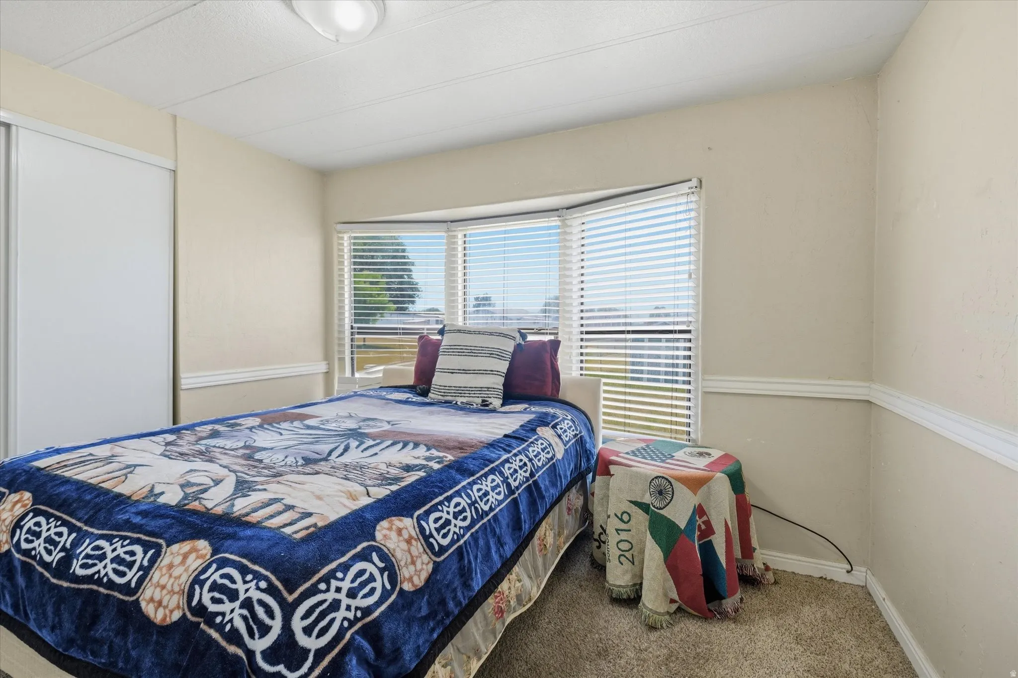 Bedroom featuring a bay window with blinds, neutral wall paint, white trim, and a sliding closet door