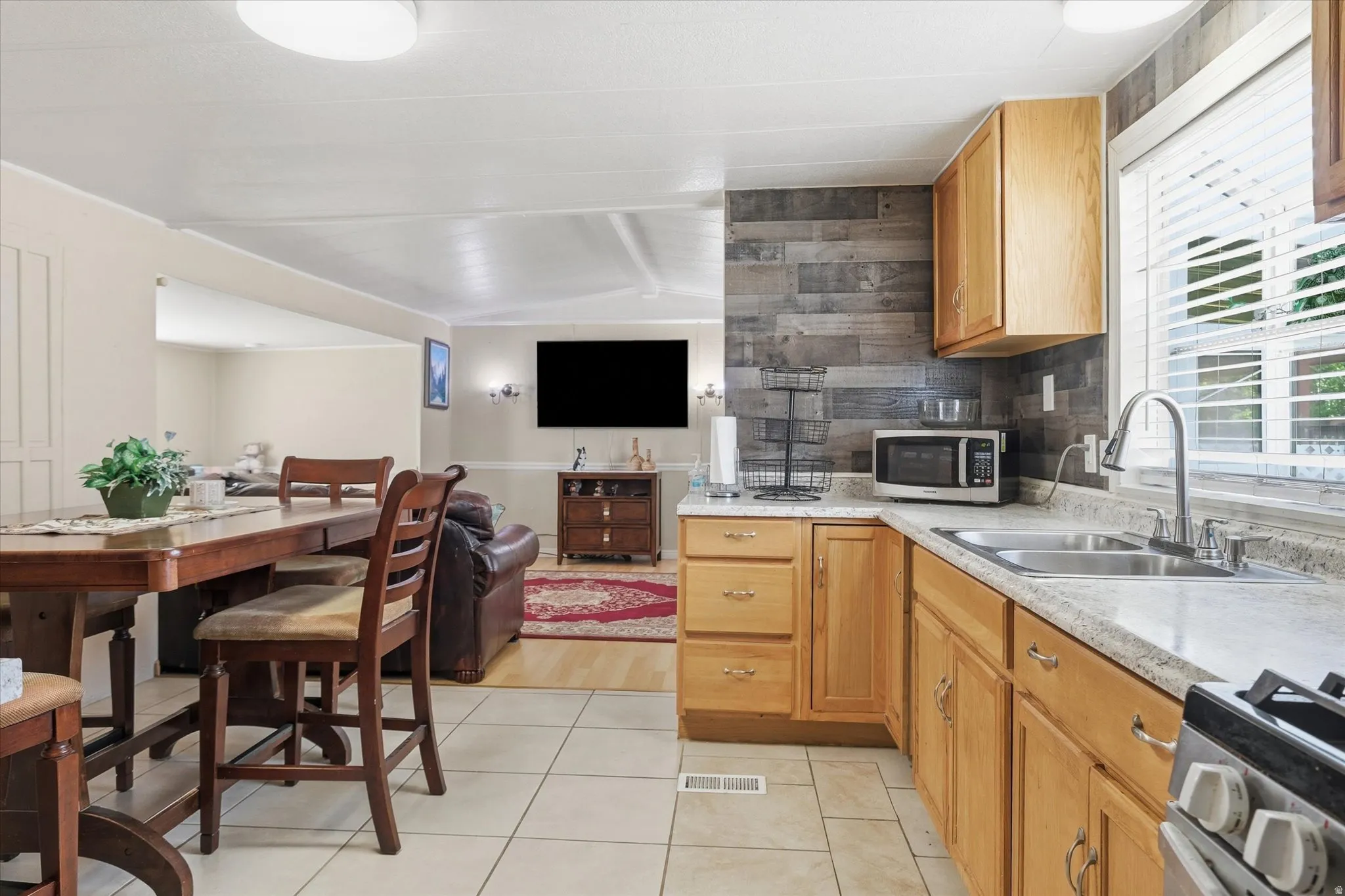Kitchen featuring light wood cabinetry, a double basin stainless steel sink, and a wood-finish plank accent wall