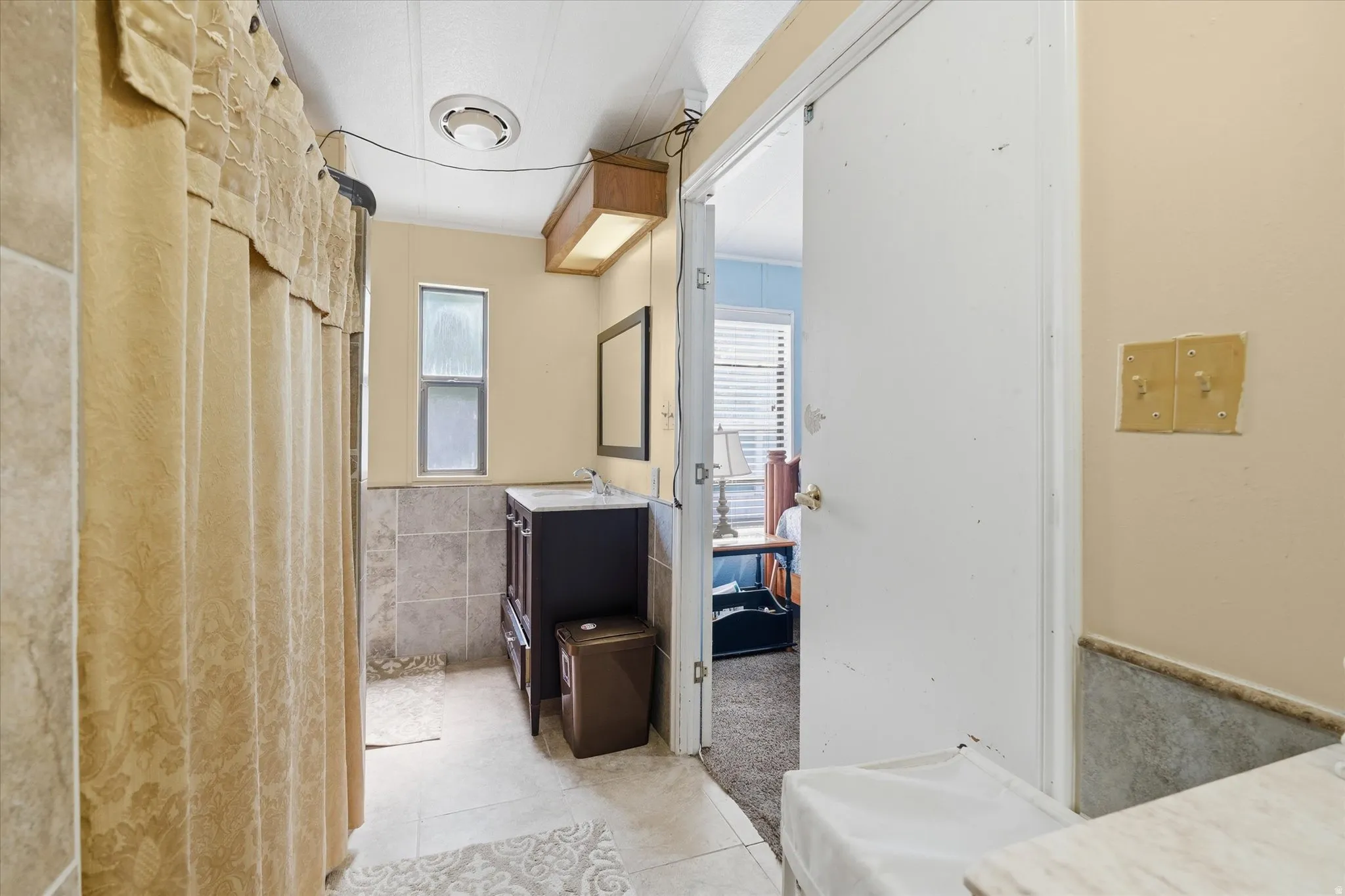 Bathroom featuring tiled flooring, a dark wood-finish vanity with an integrated sink, a rectangular mirror, and a frosted window