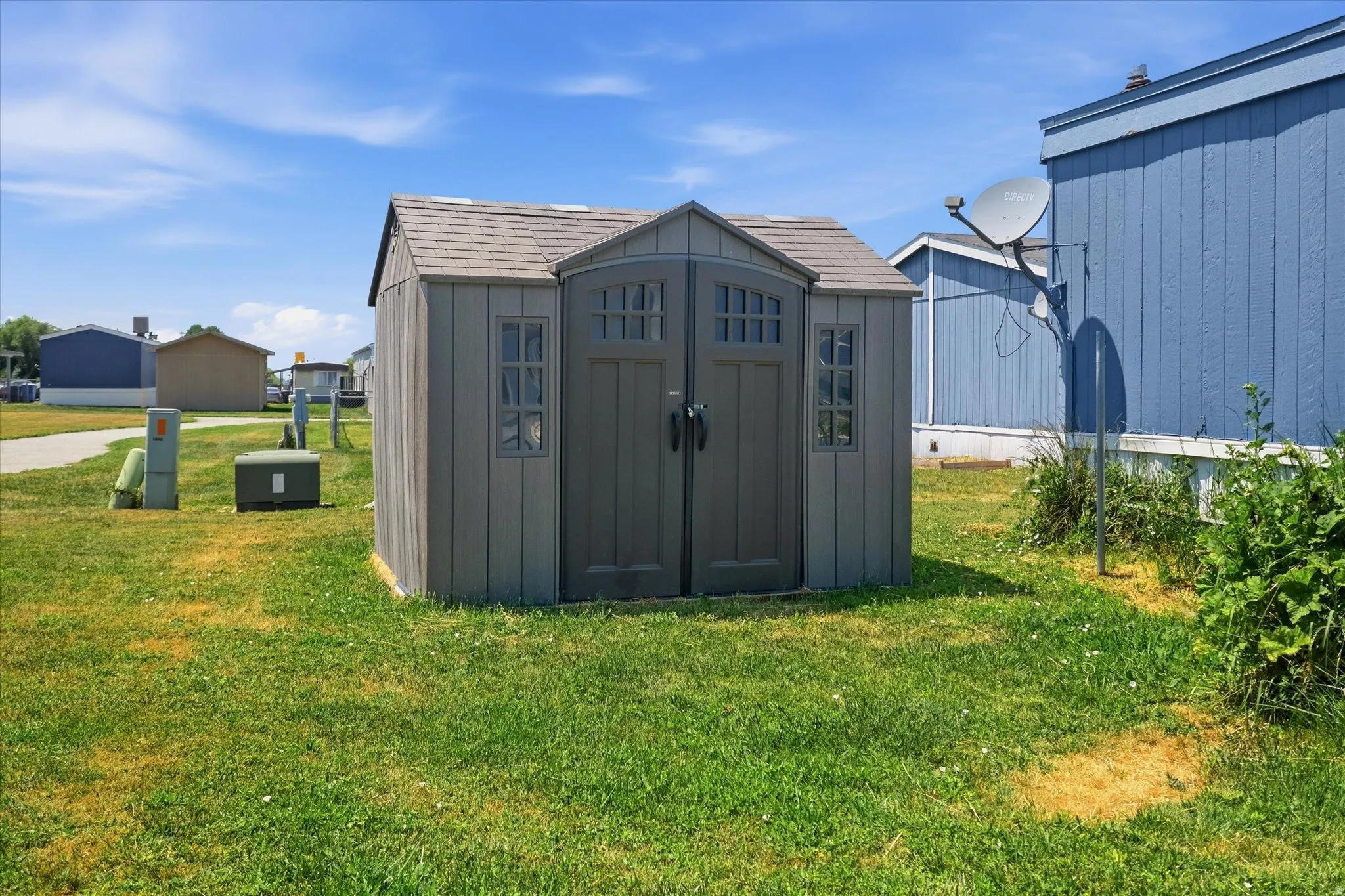 Gray storage shed with faux window details and double doors, situated on a grassy lot