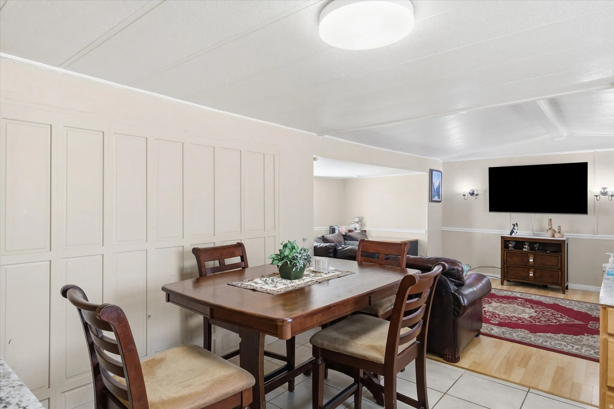 Dining area featuring a wood-finish table with seating for four, paneled accent wall, and a flush-mount ceiling light