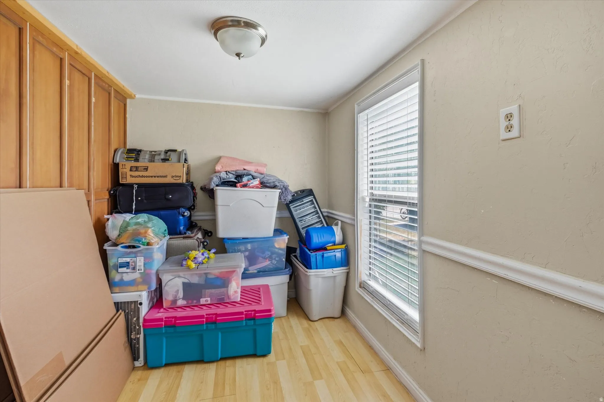 Interior room featuring built-in wood-finish cabinetry, light-toned walls, wood-finish flooring, a ceiling-mounted light fixture, and a window with blinds