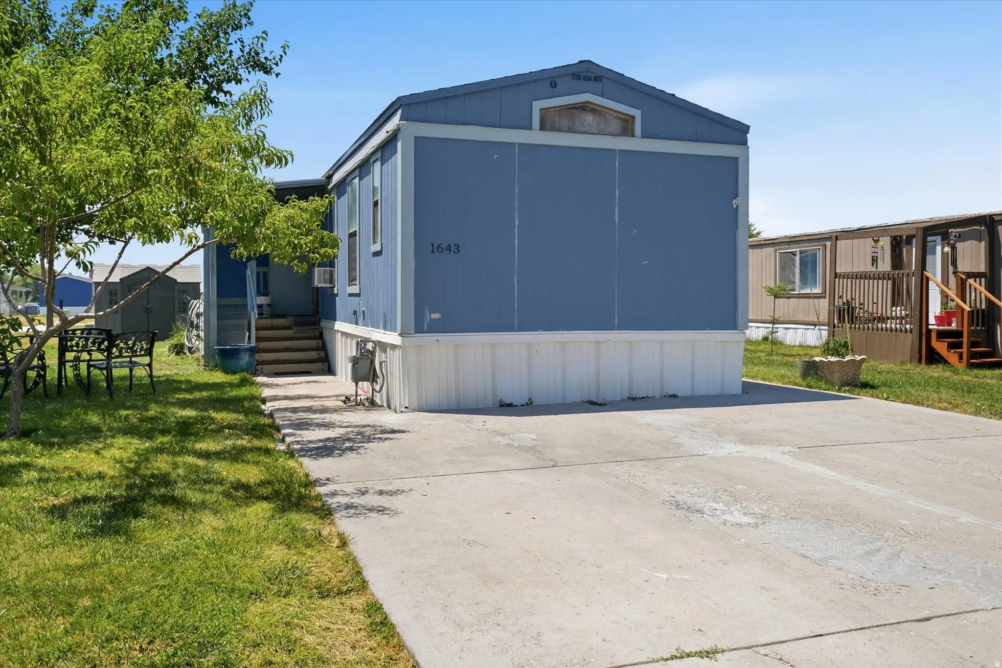 Blue exterior siding with white skirting, featuring a concrete driveway and grassy yard