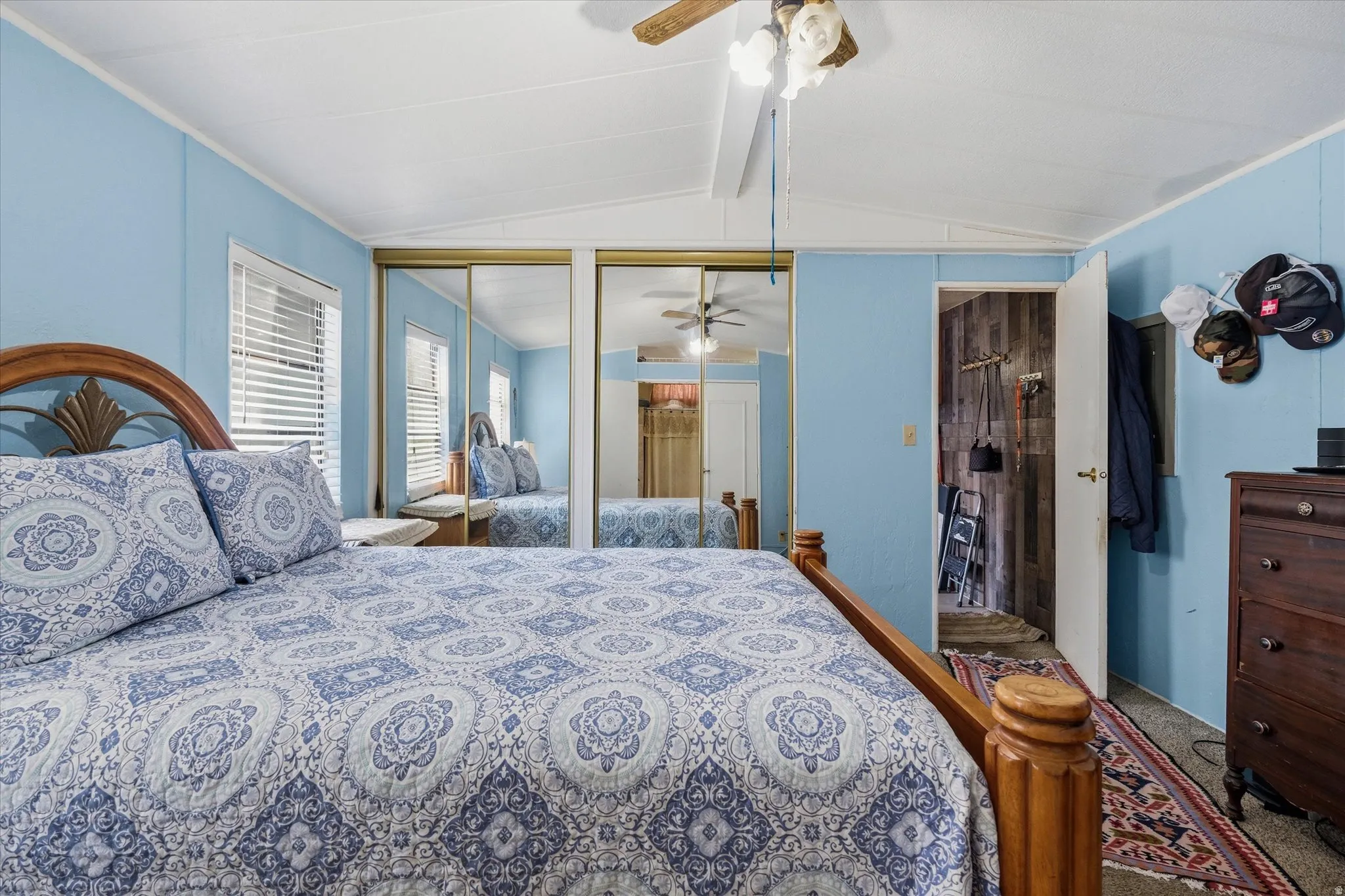 Bedroom featuring a ceiling fan, mirrored closet doors, and light blue wall panels