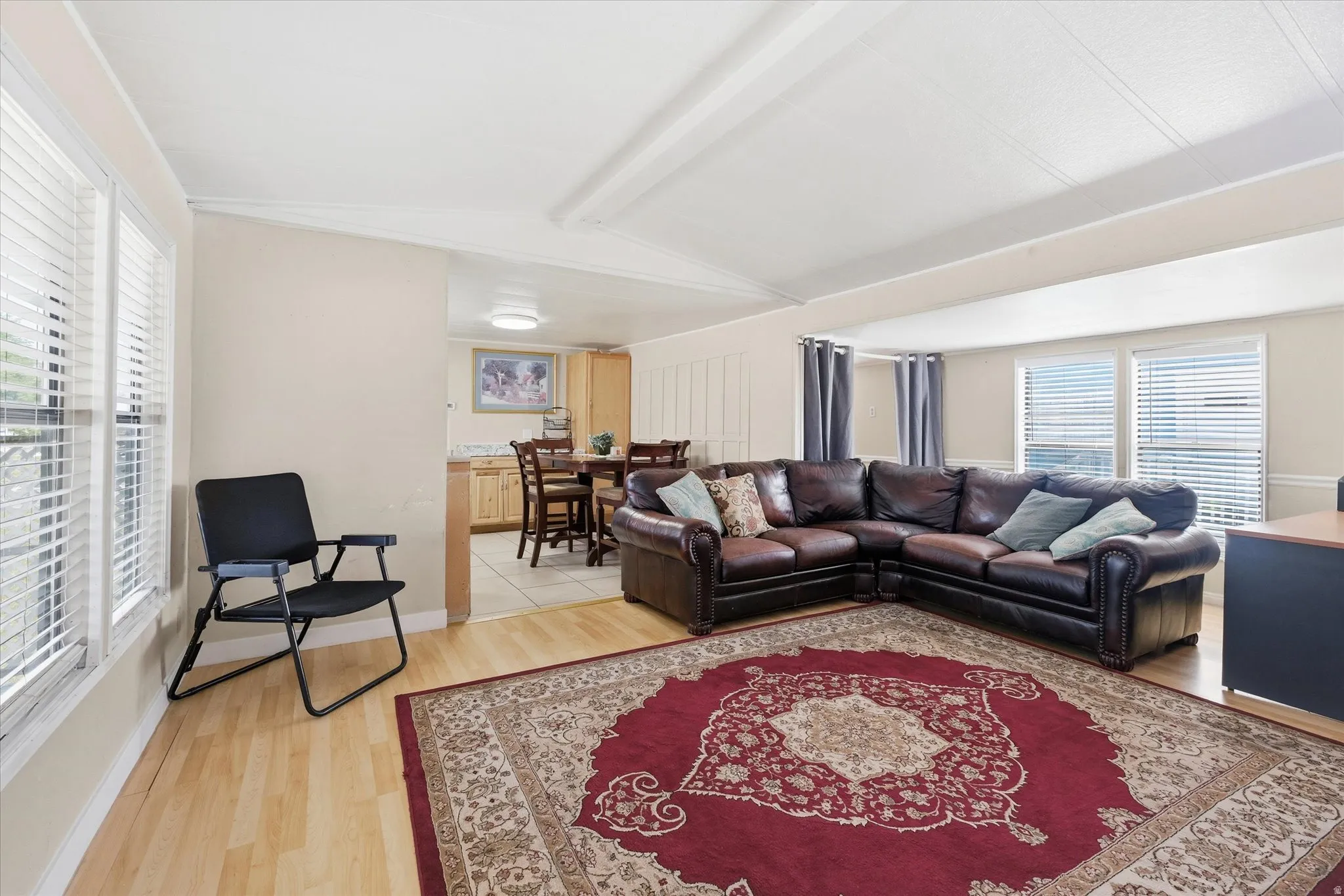 Spacious living area featuring light wood-finish flooring and multiple windows with horizontal blinds