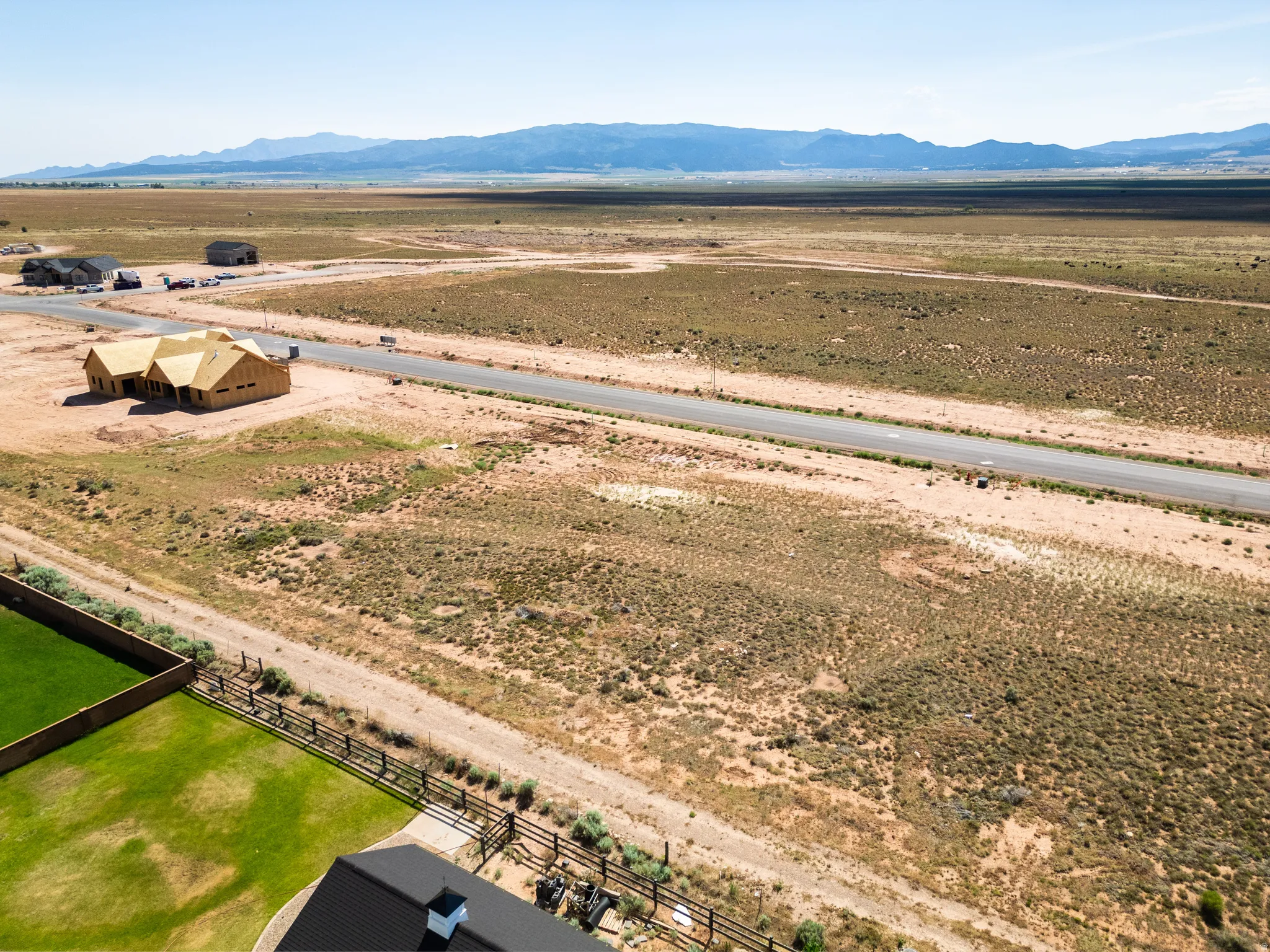 Expansive land parcel featuring a paved road, mountain backdrop, and partially constructed homes