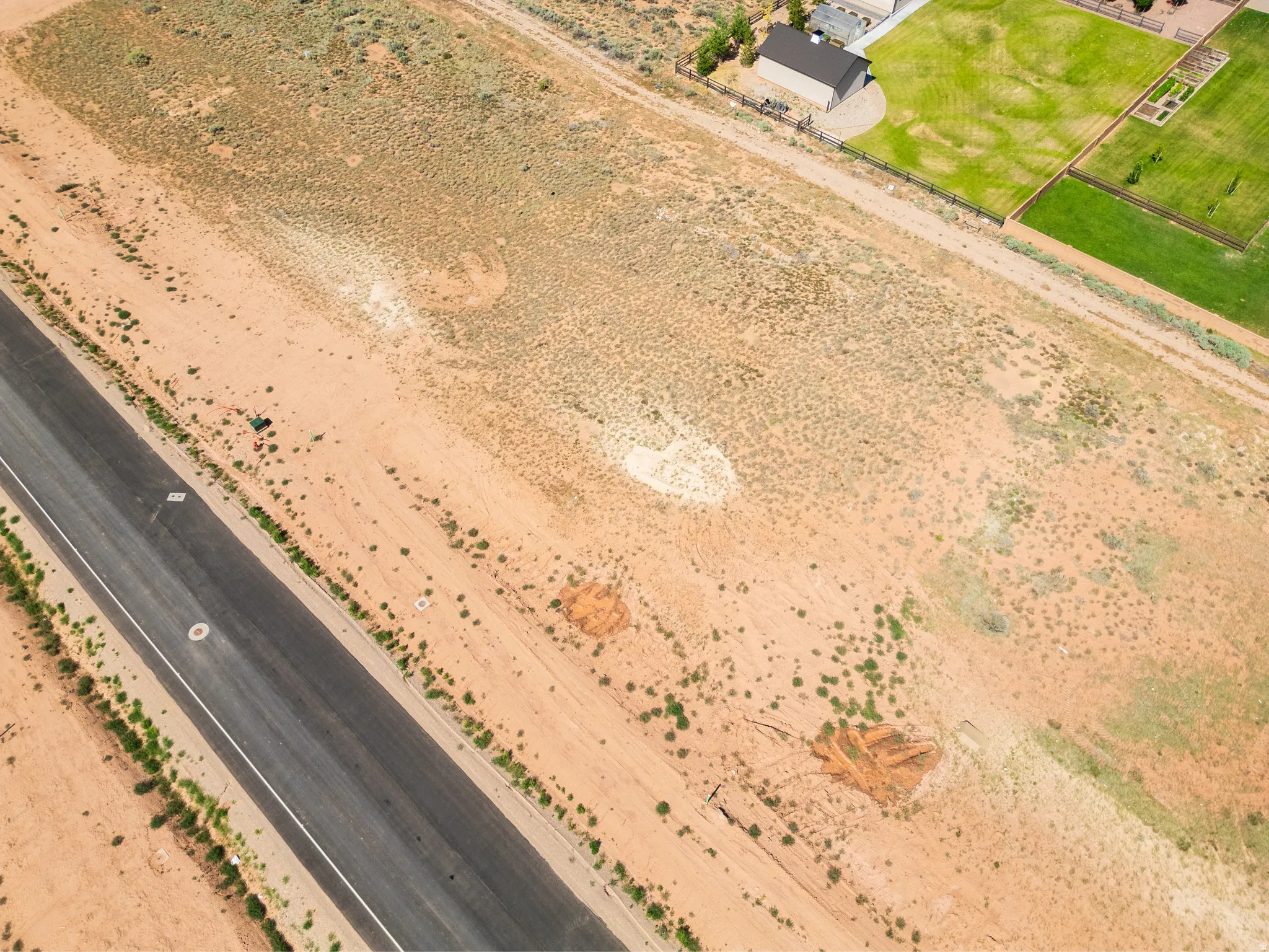 Expansive undeveloped land parcel featuring natural desert vegetation, a paved road border, and visible utility access points