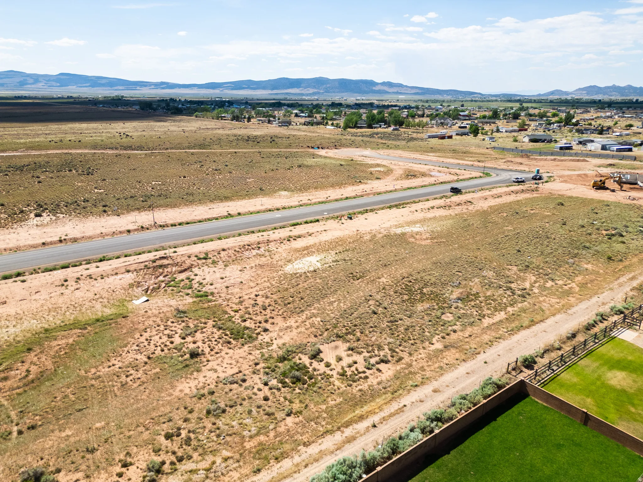 Expansive undeveloped land featuring a paved road, scattered natural vegetation, and distant mountain ranges