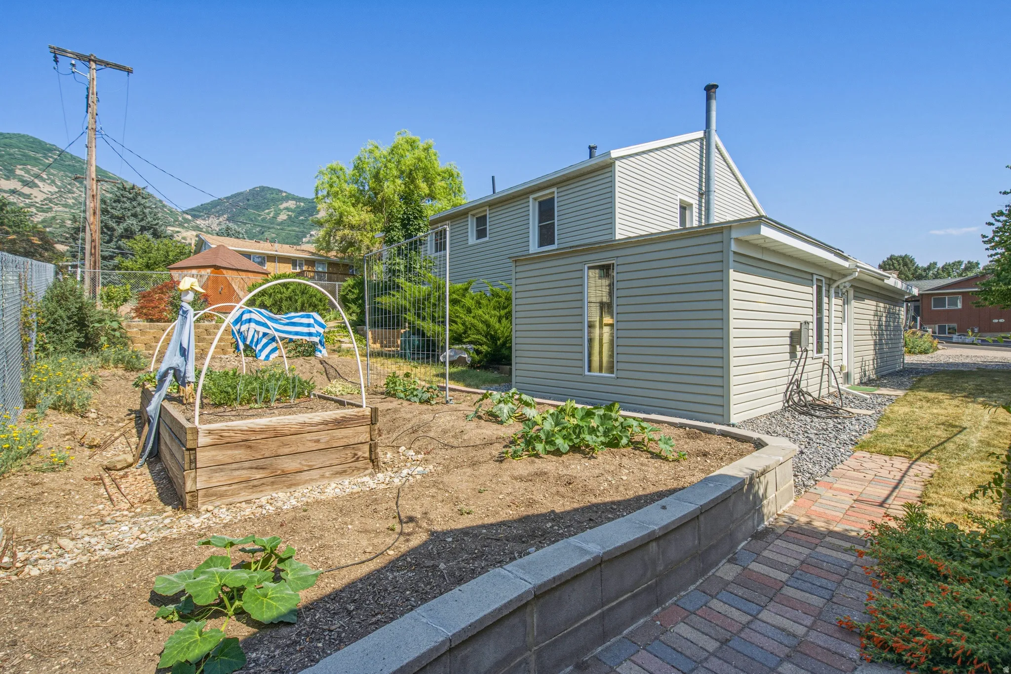 Tiered garden beds with a stone retaining wall, brick paver pathway, and side exterior entry