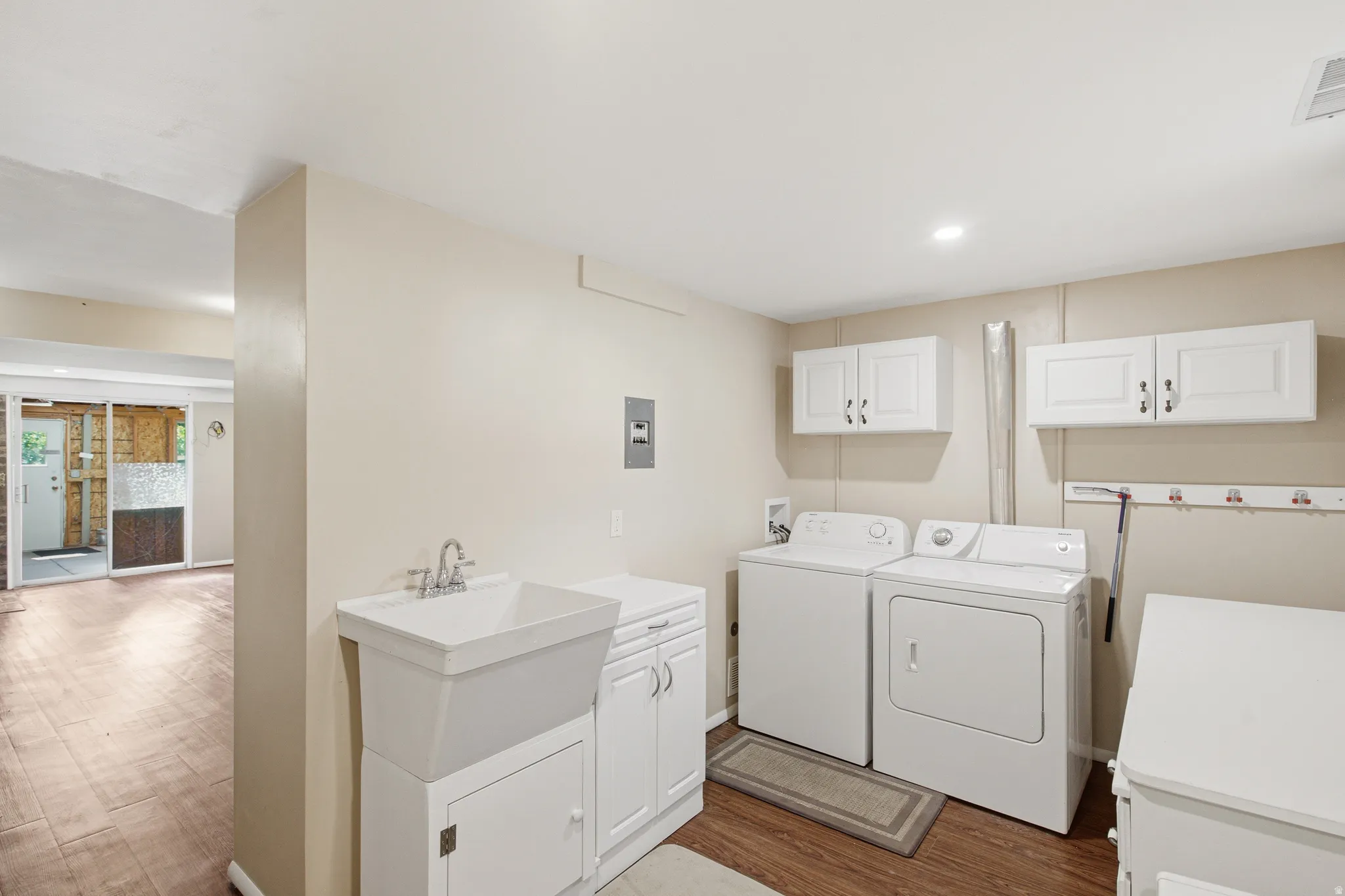 Dedicated laundry area featuring a utility sink with white cabinetry, wood-finish flooring, recessed lighting, and wall-mounted white storage cabinets