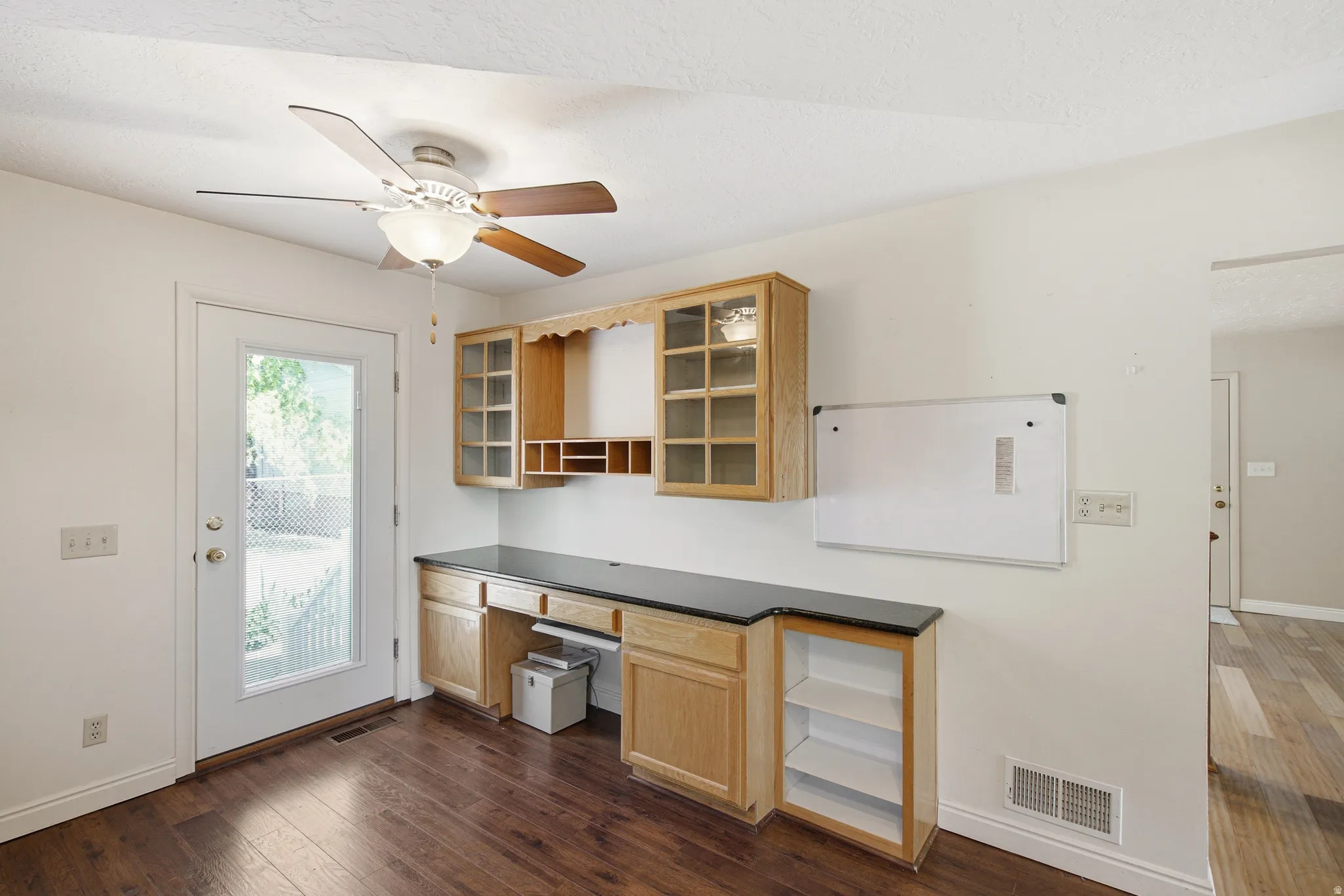 Dedicated workspace featuring built-in light wood cabinetry with glass fronts, dark countertops, and integrated desk space