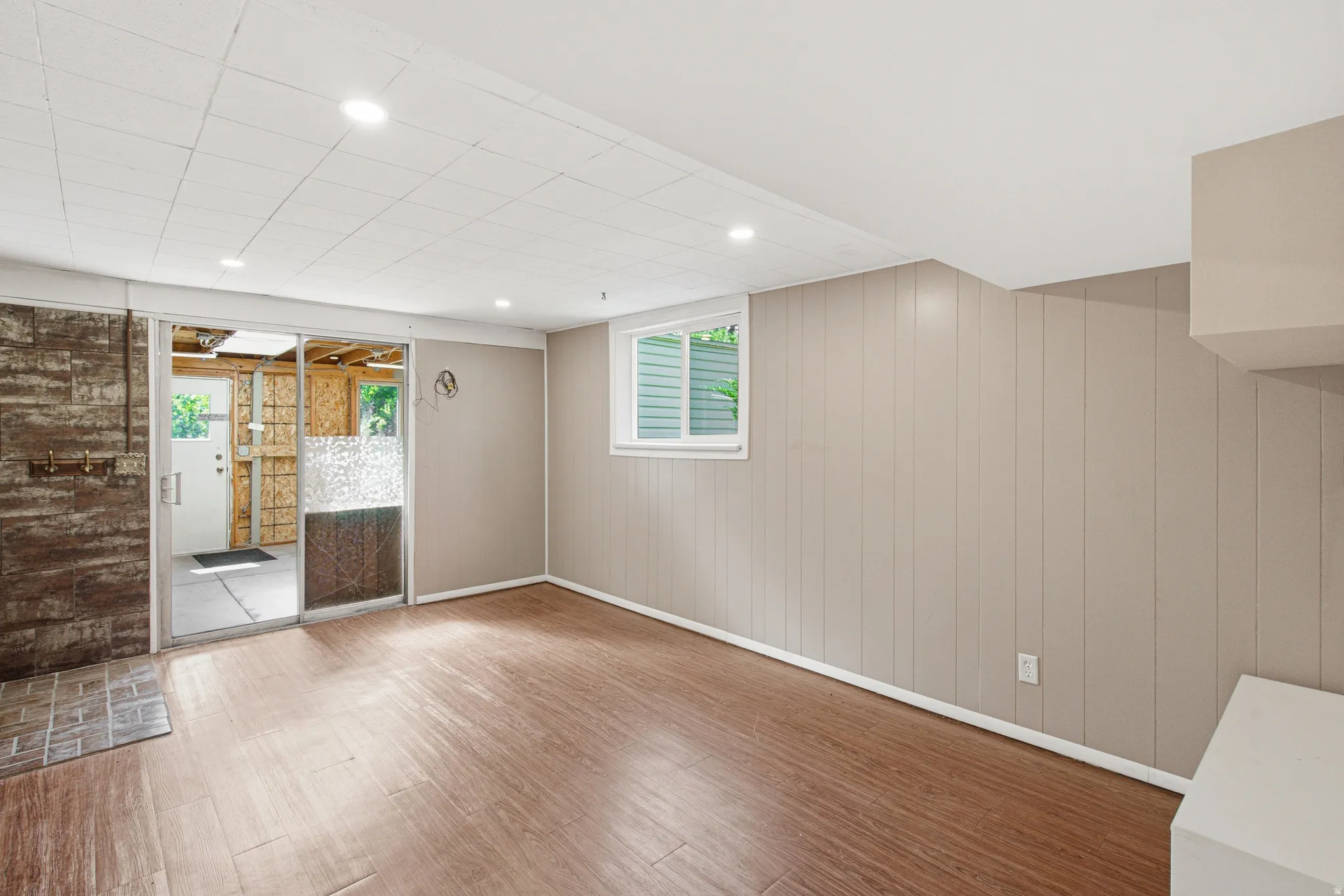 Finished lower level featuring wood-finish flooring, recessed lighting, neutral vertical paneling, and an egress window
