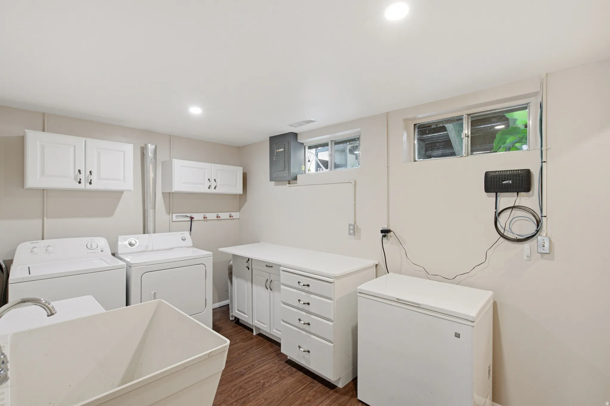 Laundry room featuring a utility sink, wood-finish flooring, two upper cabinets, lower cabinetry with drawers, and recessed lighting