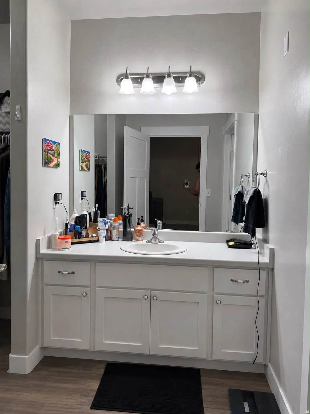 Vanity area featuring a large integrated mirror, a four-light fixture, wood-finish flooring, a white countertop, and white shaker-style cabinetry with chrome hardware